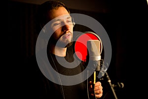 Male vocalist singing into microphone in recording studio. Creating new hit song.