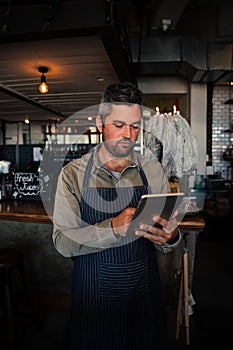 Male waiter scrolling through menu on digital tablet wearing apron in trendy cafe