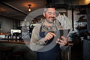 Male waiter smiling while receiving monthly salary on digital tablet in trendy cafe