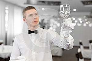 Male waiter in white gloves rubs a wine glass.