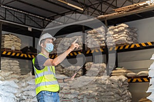 A male warehouse worker wear a mask use a laptop inspecting chemical products in alum or chemical warehouse storage. International