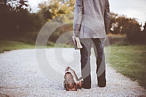 Male wearing a business suit and standing on a pathway near his suitcase while holding the bible