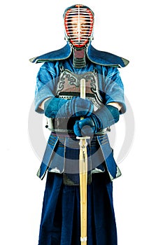 Male wearing a kendo armor with helmet and gloves holding a bamboo sword.