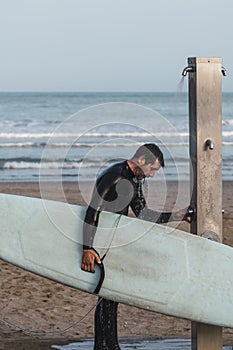 Male wearing a neoprene suit holding a surf board