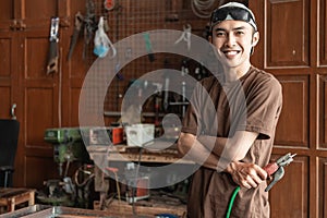 Male welder smiles with crossed hands while holding electric welder