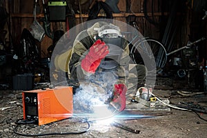 A male welder in a welding mask works with an arc electrode in his garage. Welding, construction, metal work