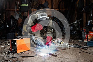 A male welder in a welding mask works with an arc electrode in his garage. Welding, construction, metal work