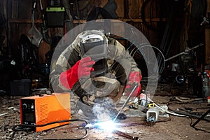 A male welder in a welding mask works with an arc electrode in his garage. Welding, construction, metal work