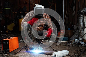 A male welder in a welding mask works with an arc electrode in his garage. Welding, construction, metal work