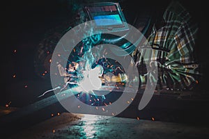 A male welder works with a welding machine in the garage, orange sparks fly to the sides