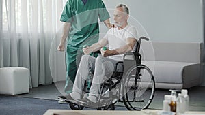 Male in wheelchair pumping his weak muscles with help of nurse, rehabilitation