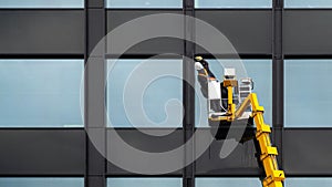 Male window cleaner cleaning glass windows on modern building high in the air on a lift platform. Worker polishing glass high in