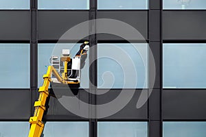 Male window cleaner cleaning glass windows on modern building high in the air on a lift platform. Worker polishing glass high in