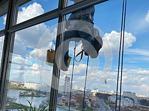 A male window washer worker, industrial climber hangs from a tall building, skyscraper and washes large glass windows for
