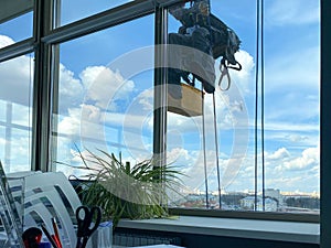 A male window washer worker, industrial climber hangs on a tall building, skyscraper and washes large glass windows for