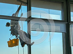 A male window washer worker, industrial climber hangs from a tall building, skyscraper and washes large glass windows for