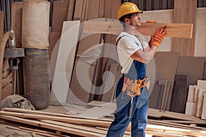 Male worker carrying timber wood plank at construction site