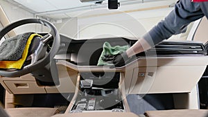 Male worker cleaning car interior with a cloth spraying a detergent on it and wiping car's dashboard.