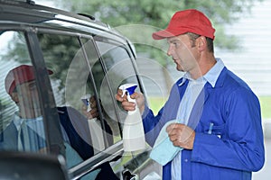 male worker cleaning car windshield with cloth and spray