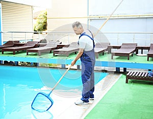 Male worker cleaning outdoor pool with net