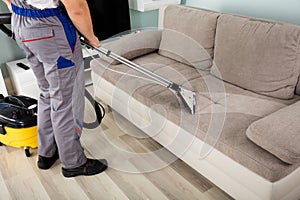 Male Worker Cleaning Sofa With Vacuum Cleaner photo