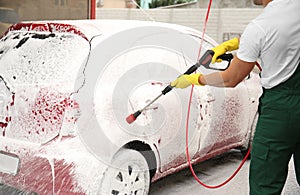 Male worker cleaning vehicle with high pressure foam