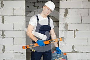 Male worker or construction worker wearing a helmet with a level, tool box, and blueprints against a brick wall