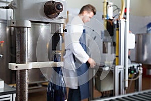 Male worker corking wine bottles with machine at sparkling wine factory