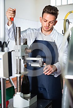 Male worker corking wine bottles with machine at sparkling wine