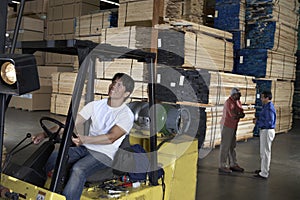 Male Worker Driving Forktruck With People In The Background