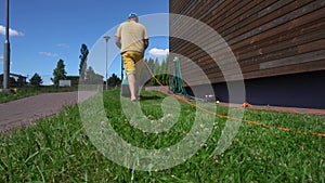 Male worker in flip-flop shoes mow grass with lawn mower. Gimbal motion shot