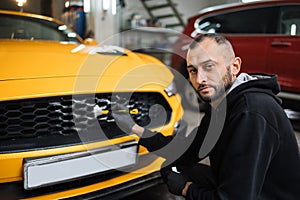 Male worker in gloves washes car radiator grille of luxury yellow car with special brush and soap