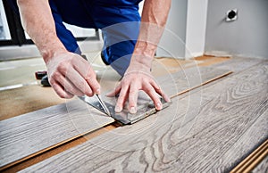 Male worker hands drawing line on laminate wood plank.