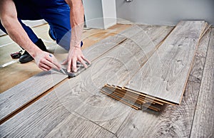 Male worker hands drawing line on laminate wood plank.