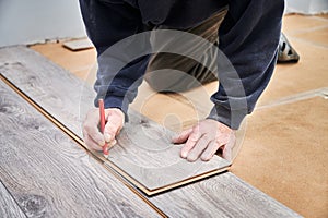 Male worker hands drawing mark on laminate plank.