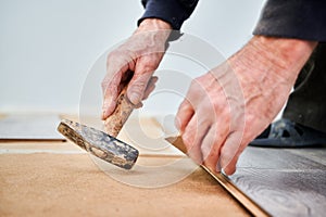 Male worker hands with hammer installing laminate flooring.