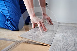 Male worker hands laying laminate flooring in apartment.