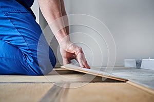 Male worker hands laying laminate flooring in apartment.