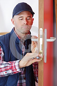 Male worker handyman carpenter at lock installation into wood door