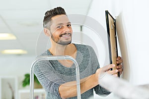 Male worker for hanging picture frame on wall at home