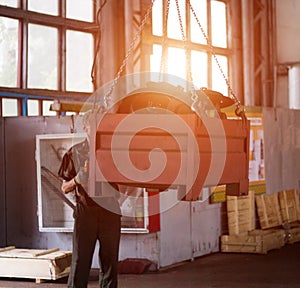 A male worker without a helmet raises the metal container of a production crane with a beam, a violation of safety precautions