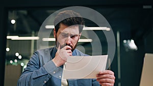 Male worker holding paper and reading with worried facial expression at office
