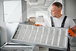 A male worker holds an air filter for air conditioning in an office space. Installation of an air conditioner.