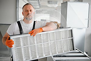 A male worker holds an air filter for air conditioning in an office space. Installation of an air conditioner.