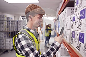 Male Worker Inside Busy Warehouse Scanning Box Barcode On Handheld Device