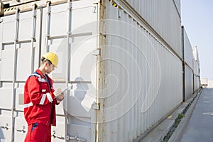 Male worker inspecting cargo container while writing on clipboard in shipping yard