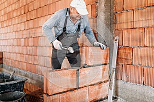 Male worker installing bricks with mortar and rubber hammer. Construction industry details