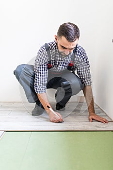 Male worker installing laminate flooring, man installing new wooden laminate flooring. Man laying laminate flooring at home. Carpe