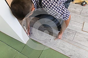 Male worker installing laminate flooring, man installing new wooden laminate flooring. Man laying laminate flooring at home. Carpe