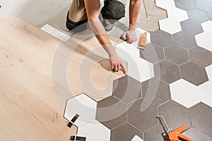 Male worker installing new wooden laminate flooring. The combination of wood panels of laminate and ceramic tiles in the